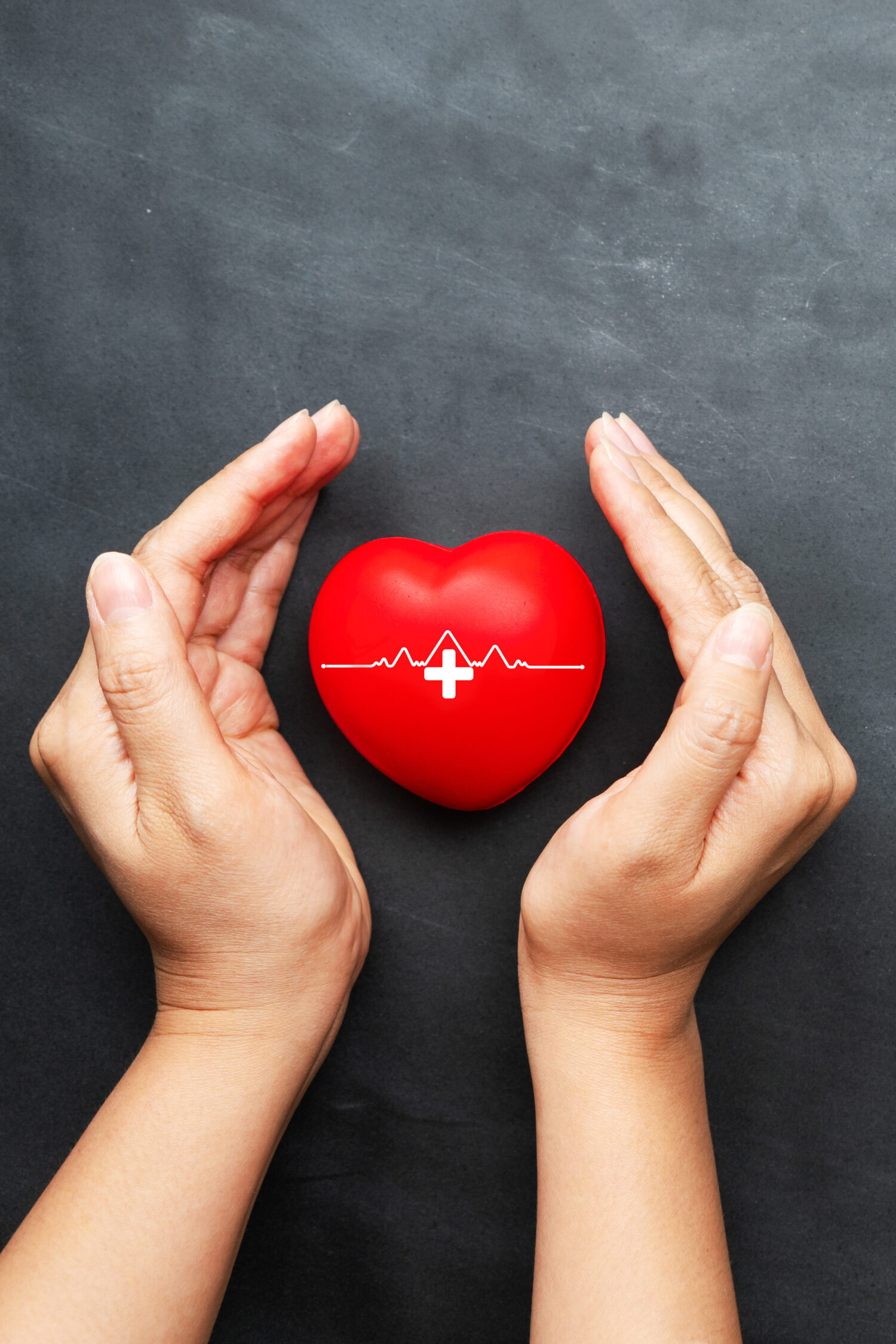 World heart day concept of young woman hand protecting red heart on black background